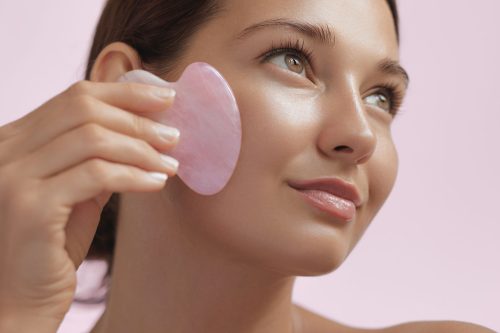 Eksperti otkrivaju kako se pravilno koristi gua sha: devojka masira lice gua sha roznekvarc kamenom