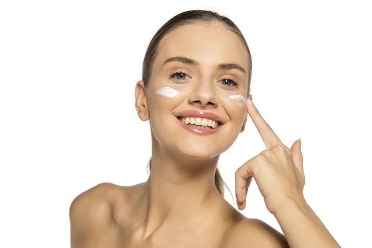 Beautiful young happy woman applies a cosmetic product on her face.