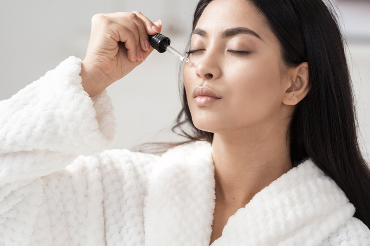 Young asian woman applying serum on facial skin