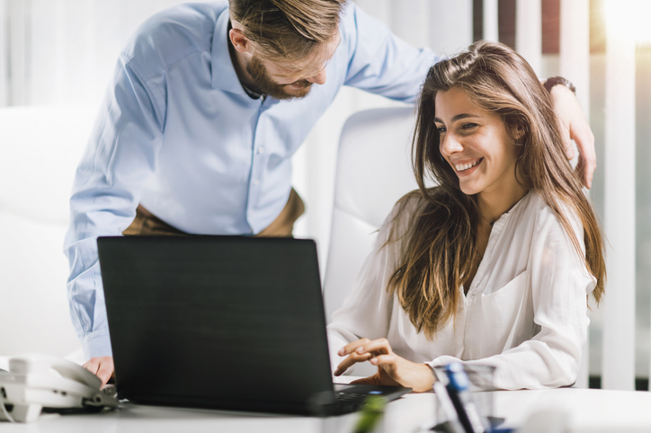 Woman Laughing With Colleague While Using Laptop On Desk In Office