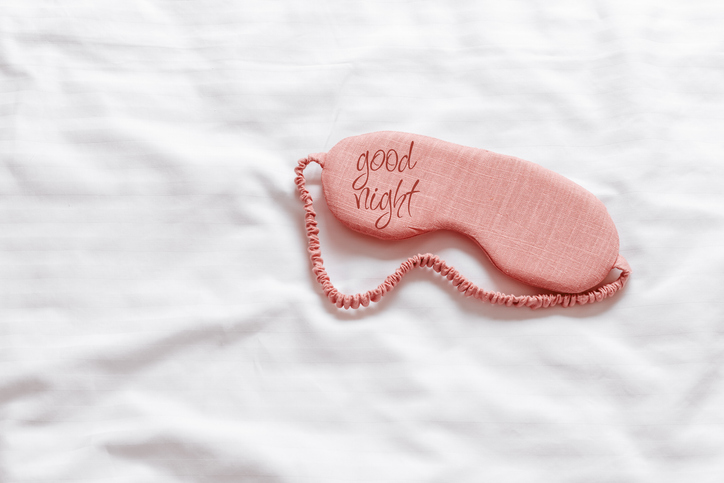 Above view pink sleep mask with text good night on white wavy cloth background. Eye cover mask for best sleep. Concept of home comfort and wellbeing, dream well, comfort rest at night. Minimal