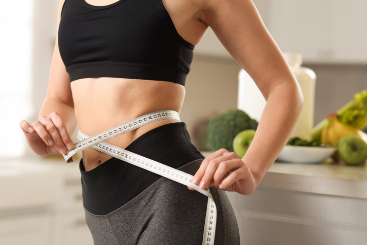 Weight loss. Woman measuring waist with tape in kitchen, closeup